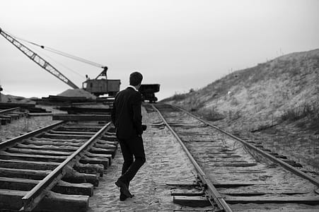 grayscale photography of man walking between railroads thumbnail