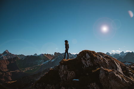 person standing on mountain cliff covered with brown grass landscape photography thumbnail