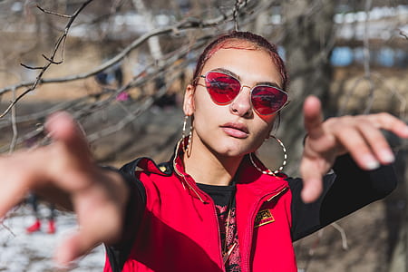 woman wearing red and black jacket and red lens sunglasses near tree thumbnail