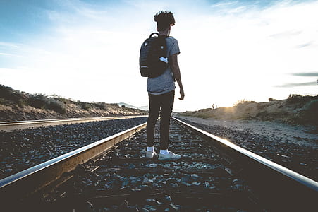 person wearing black backpack standing on railway during daytime thumbnail