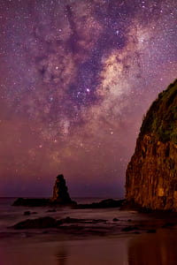 seashore beside mountain under purple and brown sky with stars thumbnail