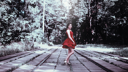 woman in red dress standing on pavement between trees photo thumbnail