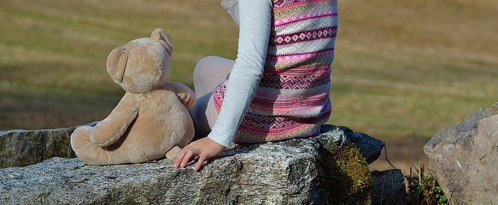 person sitting beside brown bear plush toy during daytime thumbnail