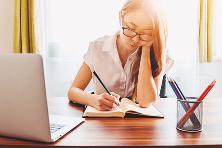 Young woman taking note and using laptop while studying at home thumbnail