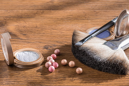 two brown and black makeup brushes near two purple and gray makeup palettes on brown wooden surface thumbnail