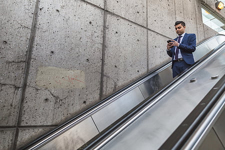man using smartphone while standing on escalator thumbnail