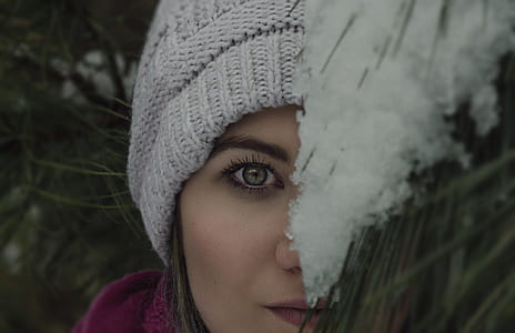 woman wearing knit cap peeking on pine tree with snow thumbnail