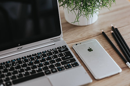 Silver Acer laptop on a wooden desk with a green plant, pencils and an Apple iPhone thumbnail