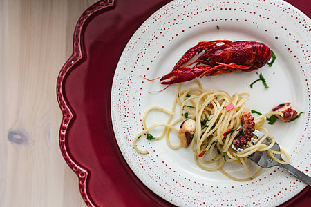 Fancy dinner with seafood pasta, crayfish and red wine by the table decorated with roses thumbnail