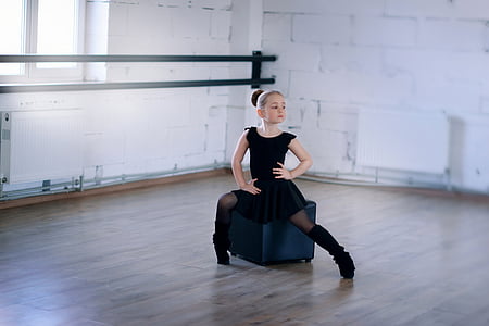 girl in black sleeveless dress sitting on blue ottoman inside building thumbnail