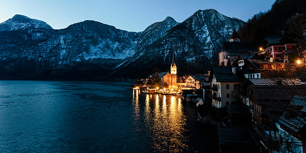lighted house beside body of water near gray mountain during golden hour thumbnail