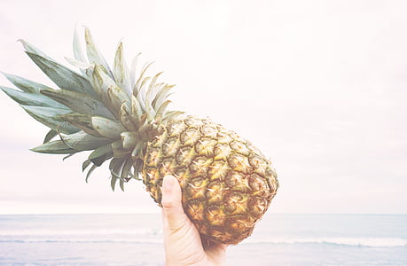 person holding pineapple in front of sea thumbnail