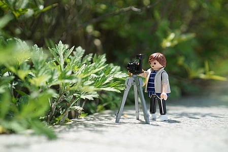 boy plastic toy with tripod camera beside green plant at daytime thumbnail