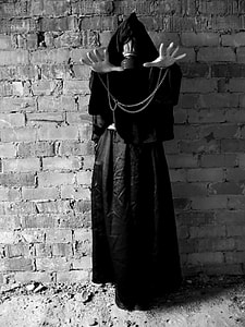 grayscale photography of person wearing black coat beside brick wall thumbnail