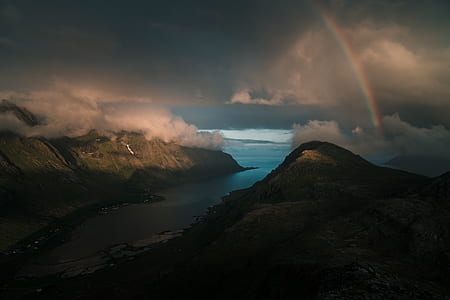 mountains and blue ocean water underneath rainbow during orange sunset thumbnail
