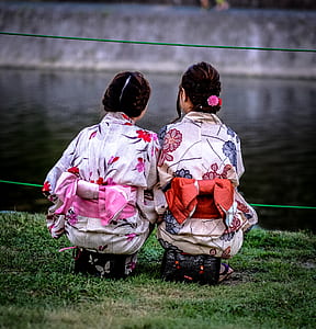 two women wearing kimonos sitting at the bank of a river thumbnail