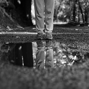 grayscale photo of man standing in front of water on ground thumbnail