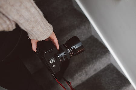 person holding black DSLR camera on stairs inside well-lit room thumbnail