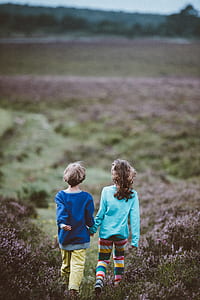 two kid walking on green grass field near mountain during daytime thumbnail