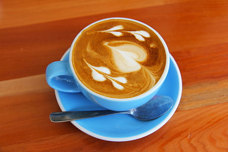 blue ceramic teacup with coffee latte and gray spoon beside on top of blue ceramic saucer thumbnail