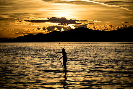 silhouette of person on boat surrounded by body of water thumbnail