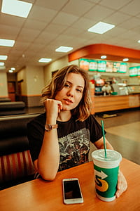 woman sitting on bench holding green disposable cup thumbnail