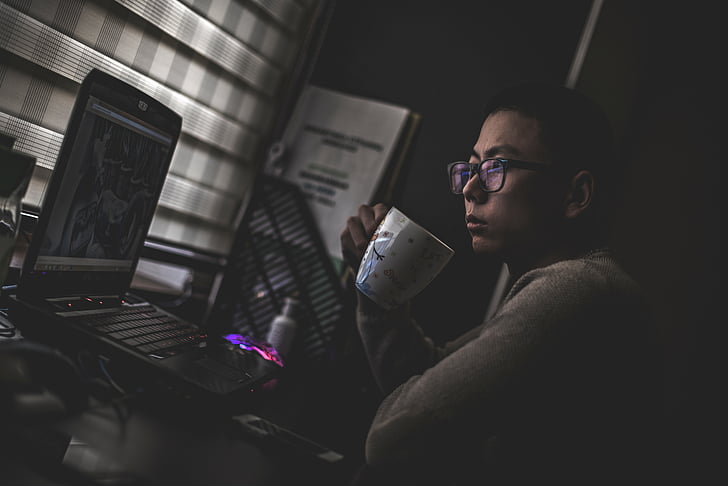 man holding cup while looking on laptop
