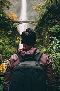 close up photography of man with backpack looking in front of waterfalls thumbnail