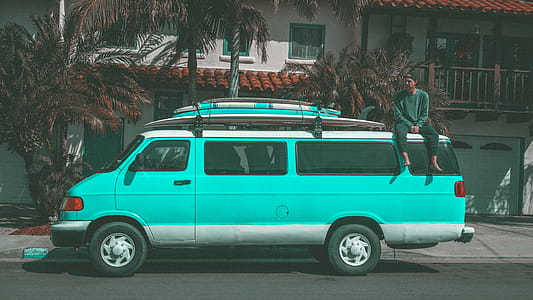 Man Sitting on Top of Teal Dodge Ram Van Parked Near House thumbnail