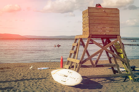 person sitting on brown wooden coast guard tower with white surfboard near beach thumbnail