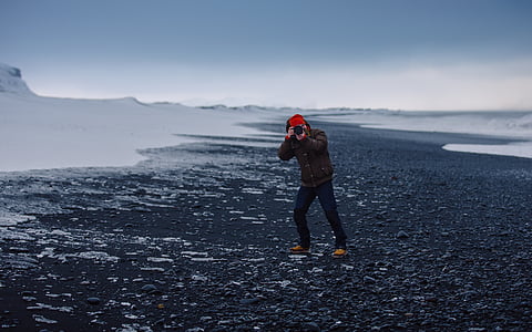 photography of man standing on the rocks pointing a camera thumbnail