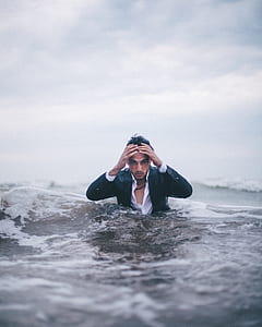 man in middle of body of water under cloudy sky thumbnail