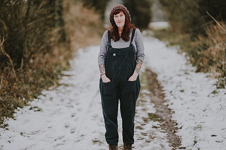 woman wearing black dungarees standing between grass during daytime thumbnail