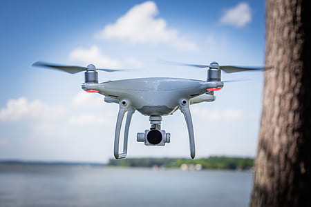 selective focus photography of white drone flying beside tree trunk thumbnail