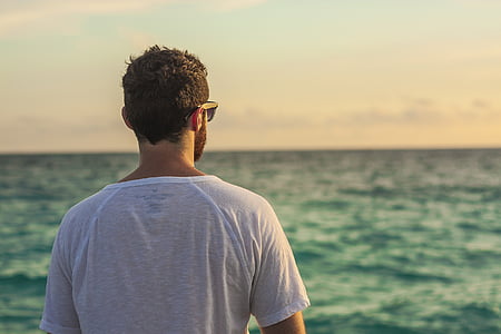 person wearing white crew-neck t-shirt while watching the body of water during daytime thumbnail