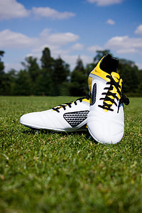 pair of white-and-yellow cleats on green grass thumbnail