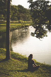 woman sitting on grass field near body of water thumbnail