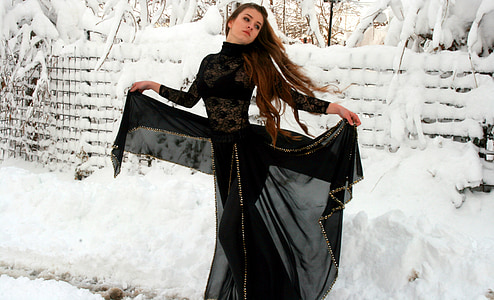 woman wearing black abaya dress opening her dress wide standing near fence covered with snow during daytime thumbnail