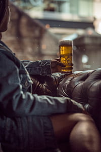 woman sitting on tufted brown leather chair holding pilsner glass filled with beer thumbnail