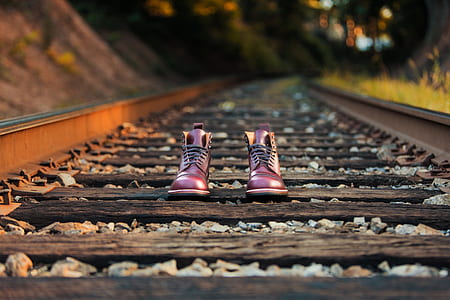 pair of brown leather boots on train rails during daytime thumbnail