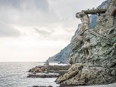 man holding bridge statue on cliff near body of water thumbnail