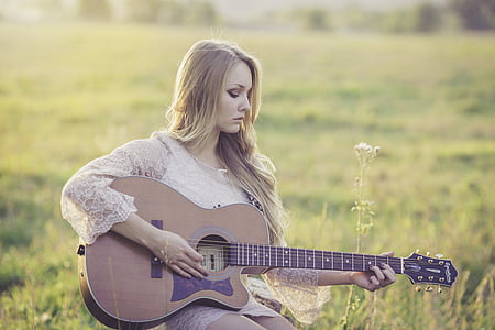 shallow focus photography of woman playing cutaway acoustic guitar thumbnail