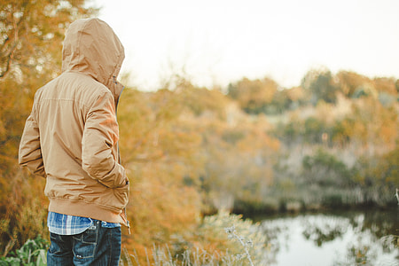 man wearing brown hooded jacket beside tree thumbnail