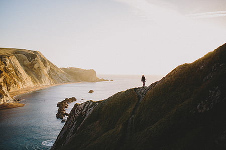 person standing on mountain near body of water thumbnail