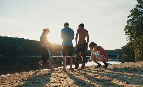 four men standing near body of water during daytime thumbnail
