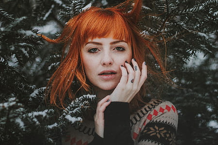 woman with red hair wearing black, gray, and red sweater near tree during snow season thumbnail