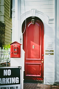red fire alarm on white house beside red door closeup photography during daytime thumbnail