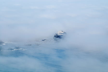 bird's-eye view photography of white island in ocean with smoke thumbnail