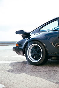 Side view of a black sports car rear wheel and spoiler in the day time thumbnail