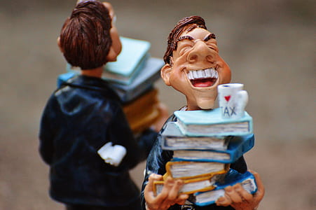 selective focus photography of man carrying pile of books figurine thumbnail